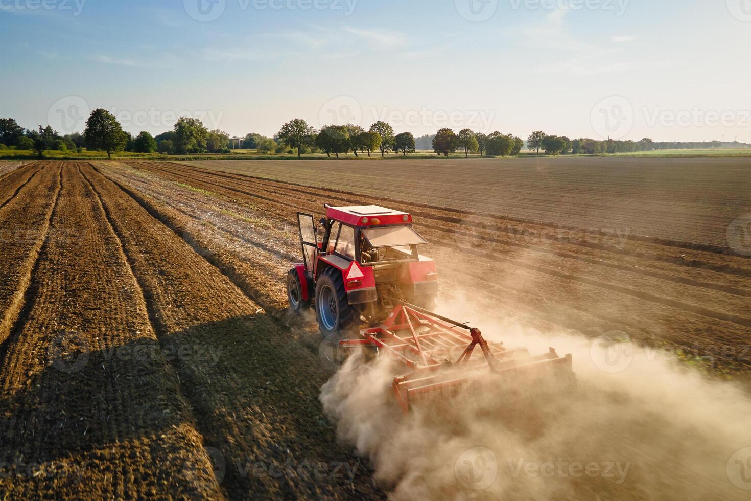 Red tractor working in agricultural field, cultivating and plowing dry soil, aerial view. Agribusiness concept. Small farming concept photo