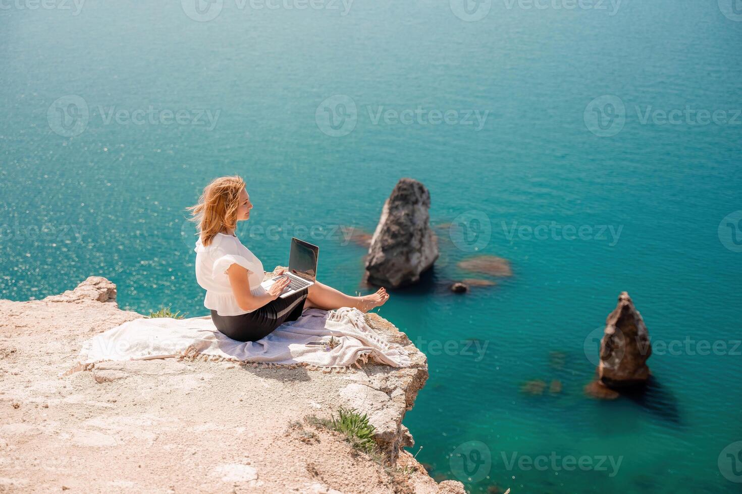 Freelance woman working on a laptop by the sea, typing away on the keyboard while enjoying the beautiful view, highlighting the idea of remote work. photo