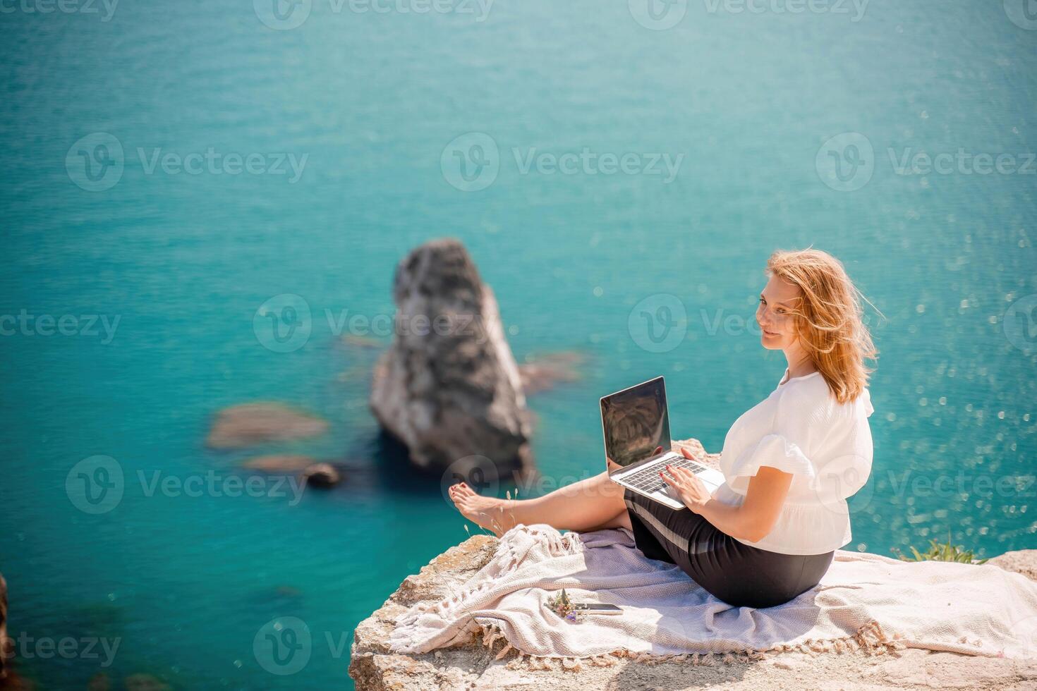 Freelance woman working on a laptop by the sea, typing away on the keyboard while enjoying the beautiful view, highlighting the idea of remote work. photo