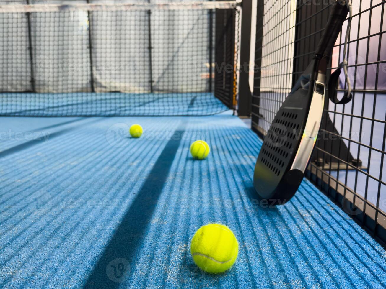 Padel racket and yellow ball behind net on a green court grass turf outdoors at sunset. Paddle is a racquet game. Professional sport concept with space for text photo