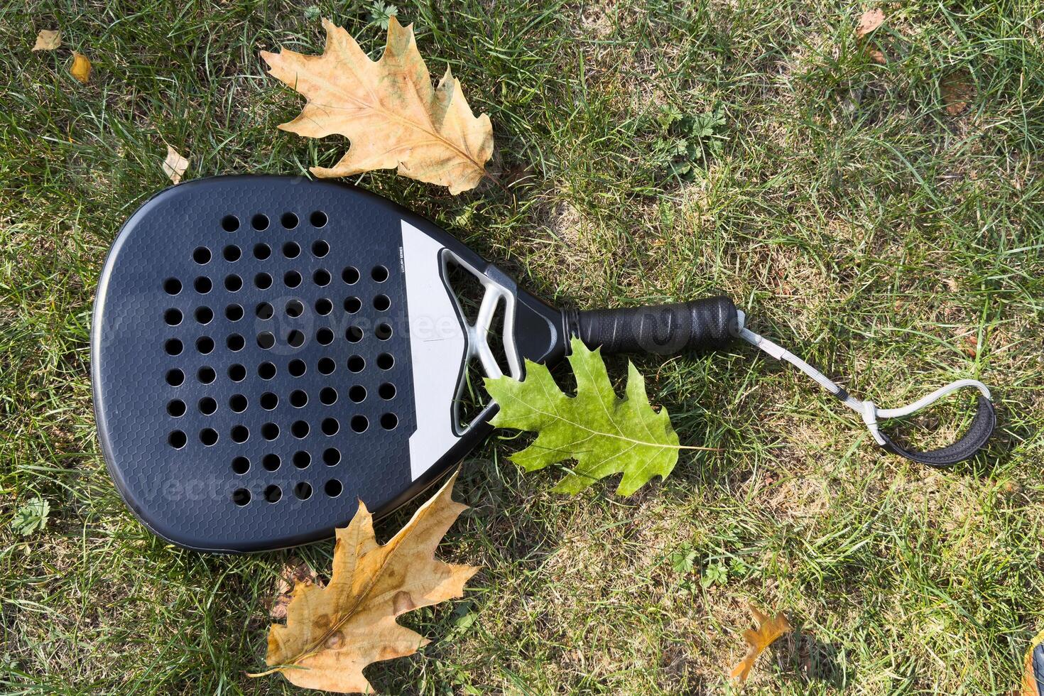 Top view of a black padel racket on a green court grass turf behind the net outdoors. Paddle is a racquet game. Professional sport concept with space for text photo