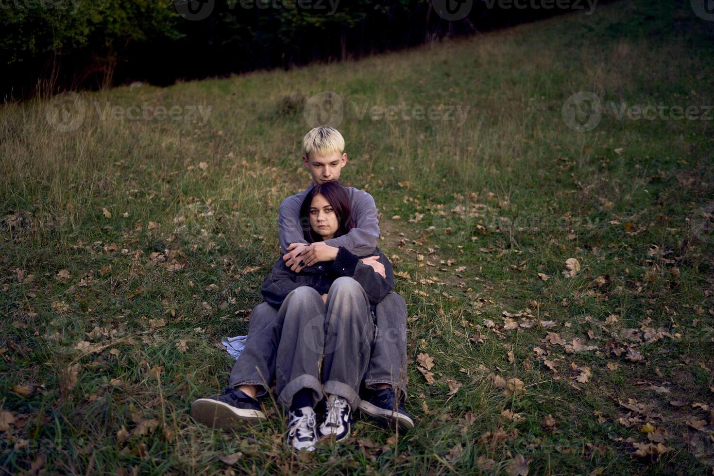 15-year-old teenage couple in love lies, sits on the grass in the park surrounded by fallen autumn leaves photo