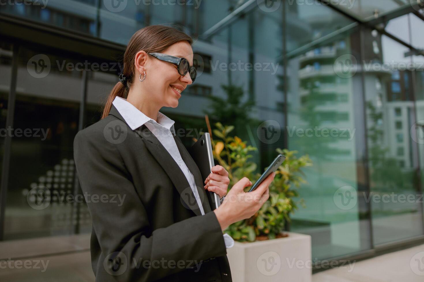 Businesswoman showing tech skills with smartphone outdoors in corporate setting photo