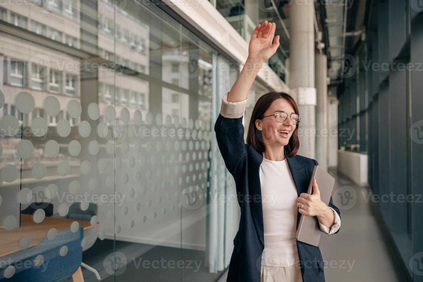 A businesswoman waves in a modern office, showing professionalism and positivity photo