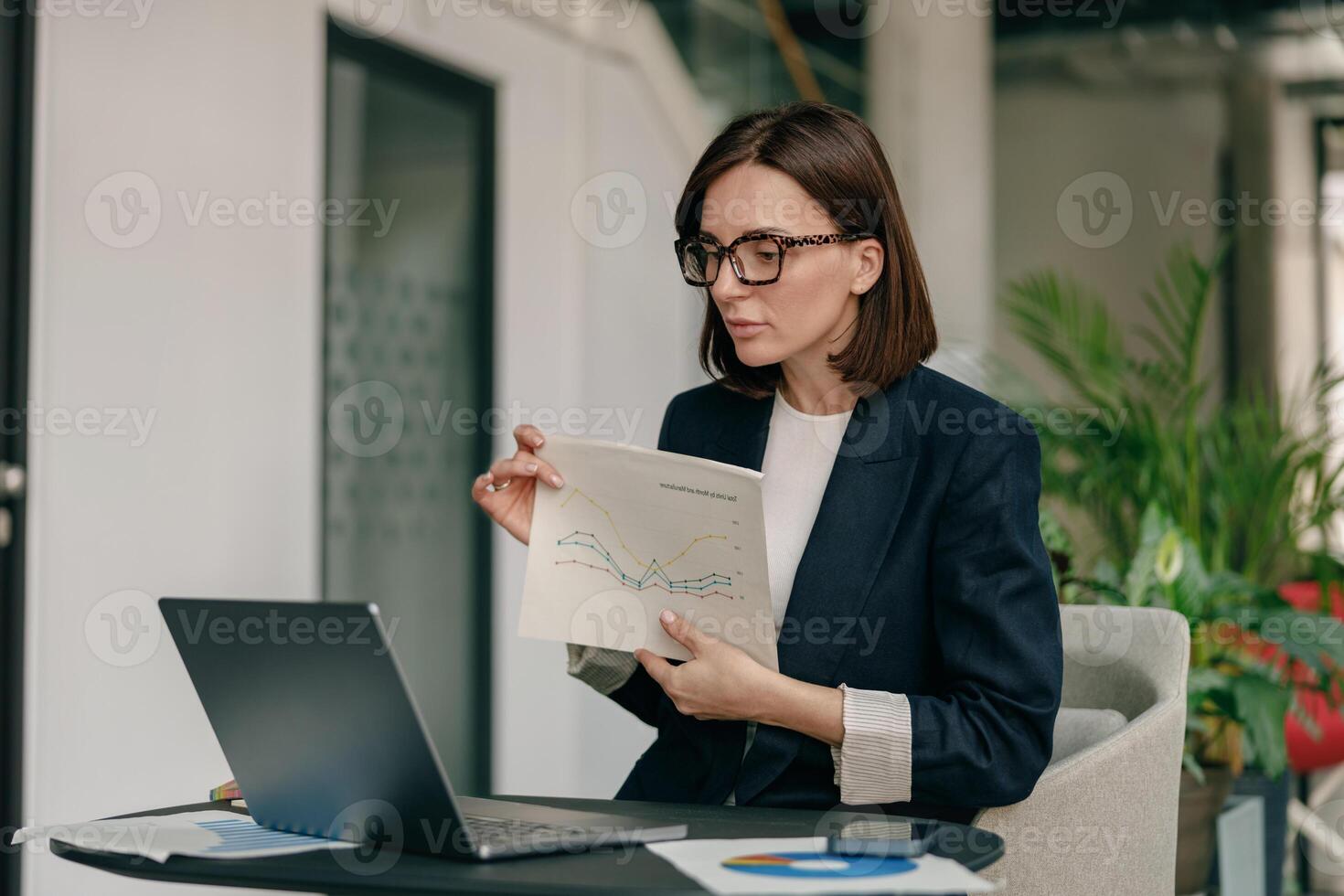 A businesswoman is focused on analyzing financial reports in a modern office setting photo