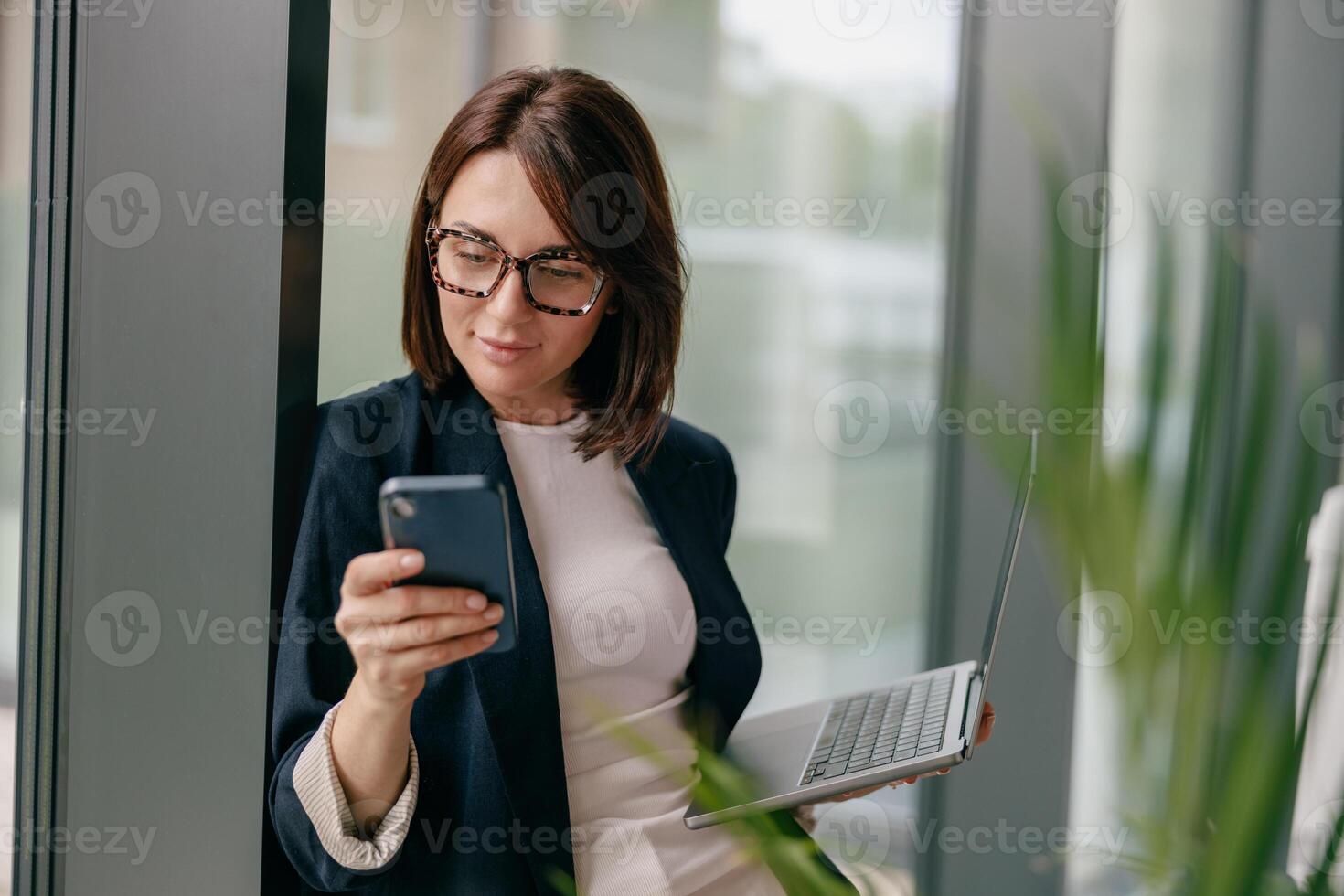 A young businesswoman in an office multitasking with a smartphone and laptop for work photo