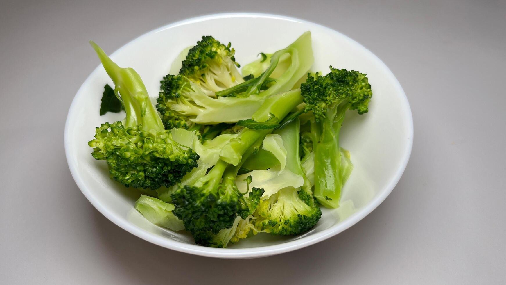 Cooked broccoli in a white bowl on a grey background, close up photo