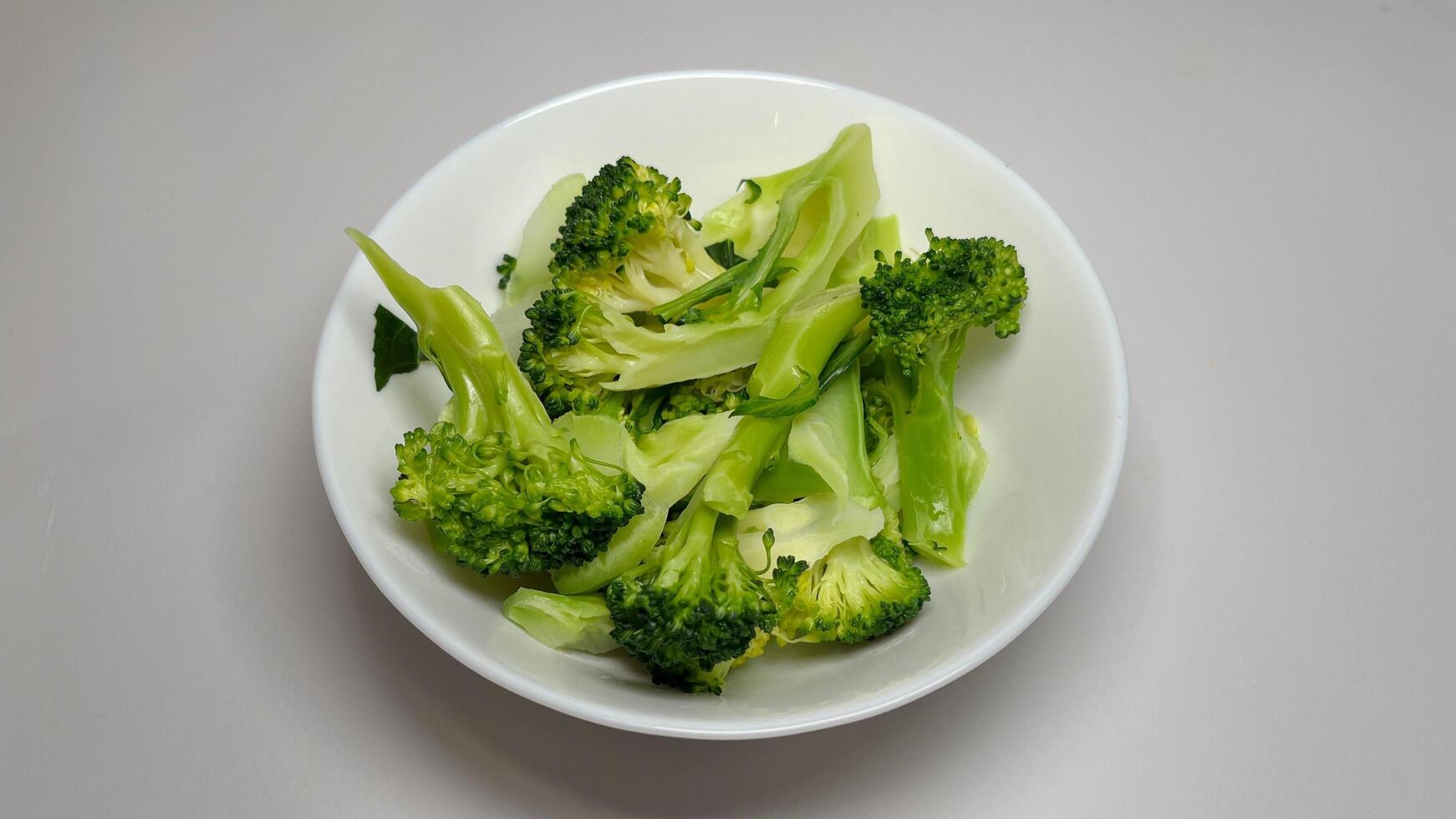 Cooked broccoli in a white bowl on a grey background, close up photo