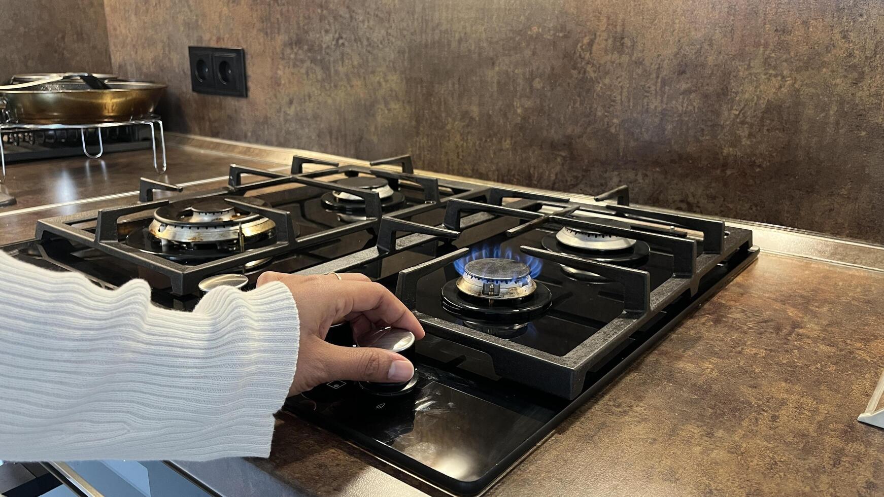 Woman's hand turns on a gas stove in a modern kitchen. photo