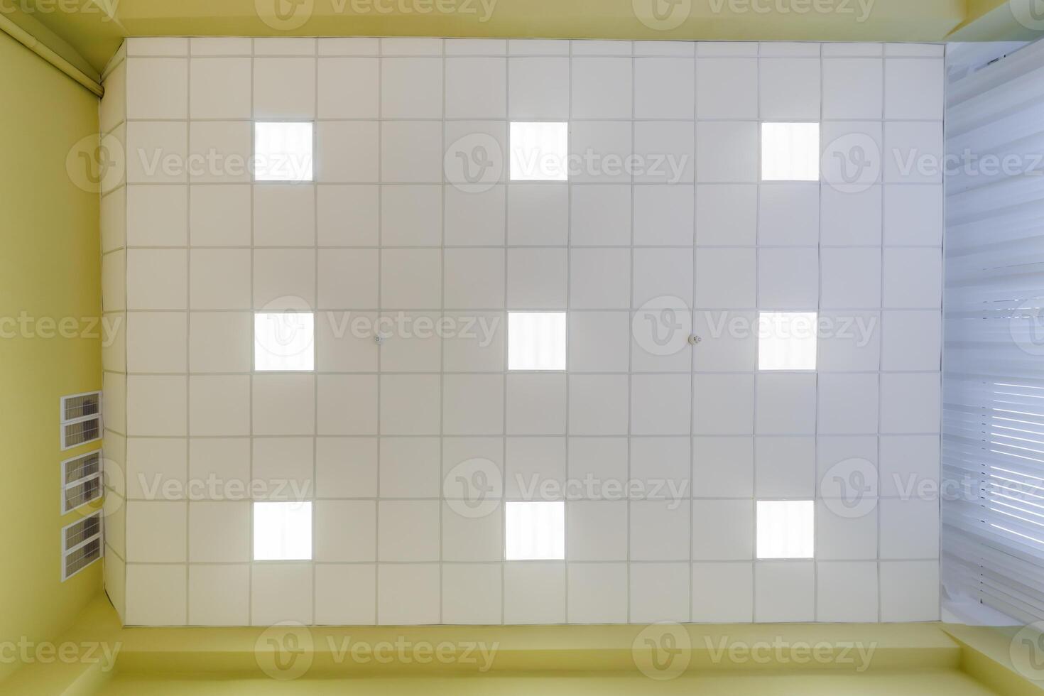 cassette stretched or suspended ceiling with square halogen spots lamps and drywall construction in empty room in house or office. Looking up view photo