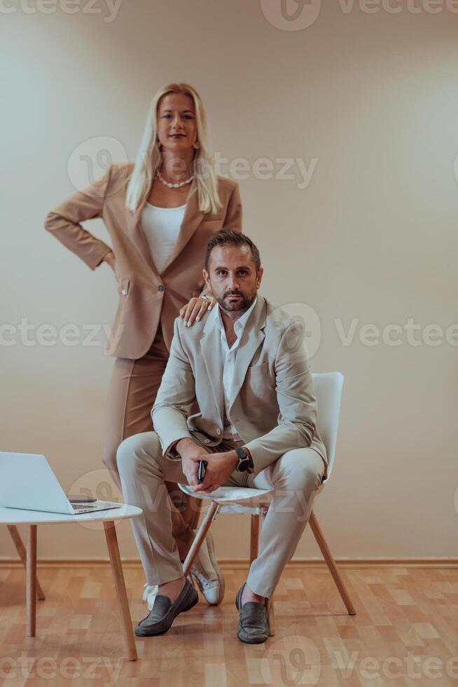 A business couple posing for a photograph together against a beige backdrop, capturing their professional partnership and creating a timeless image of unity and success. photo