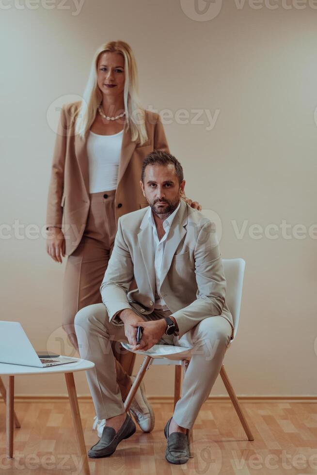 A business couple posing for a photograph together against a beige backdrop, capturing their professional partnership and creating a timeless image of unity and success. photo