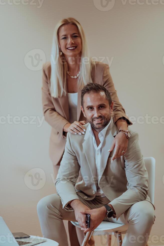 A business couple posing for a photograph together against a beige backdrop, capturing their professional partnership and creating a timeless image of unity and success. photo