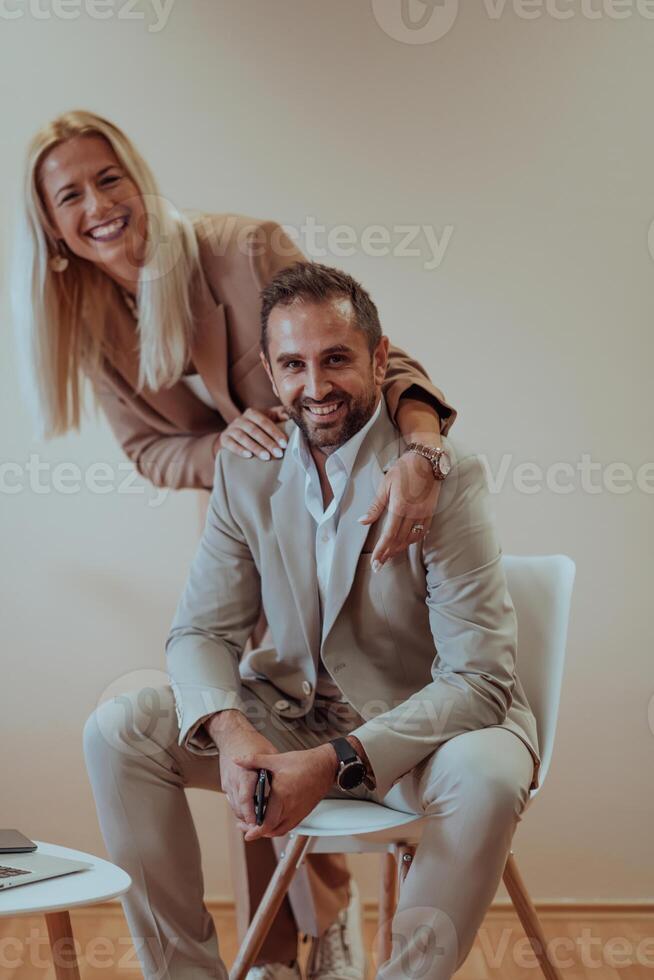 A business couple posing for a photograph together against a beige backdrop, capturing their professional partnership and creating a timeless image of unity and success. photo