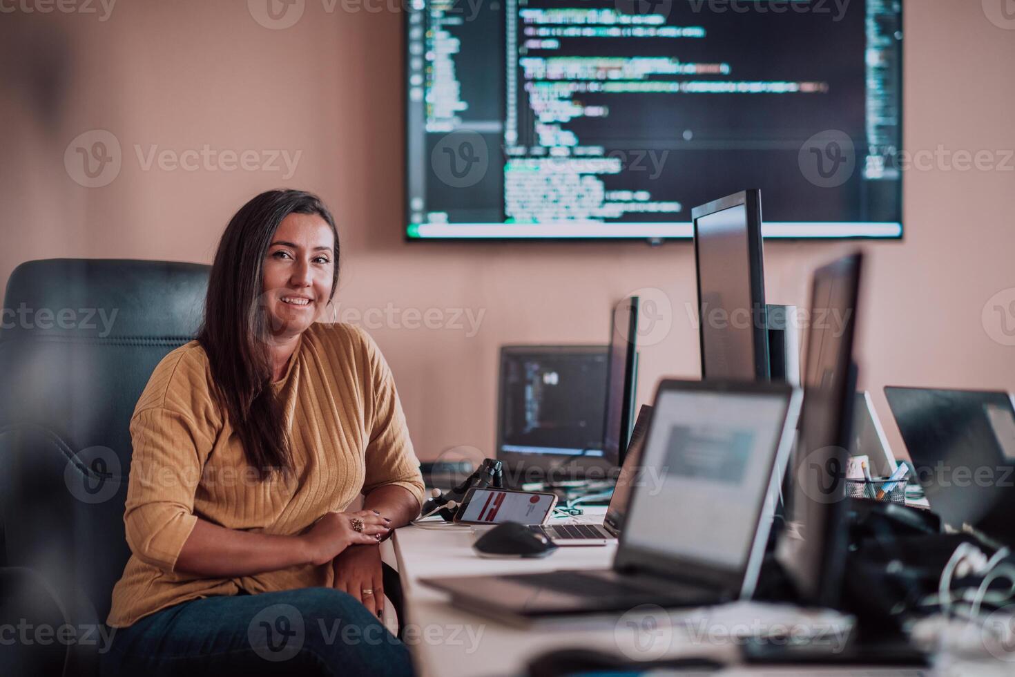 A businesswoman sitting in a programmer's office surrounded by computers, showing her expertise and dedication to technology. photo