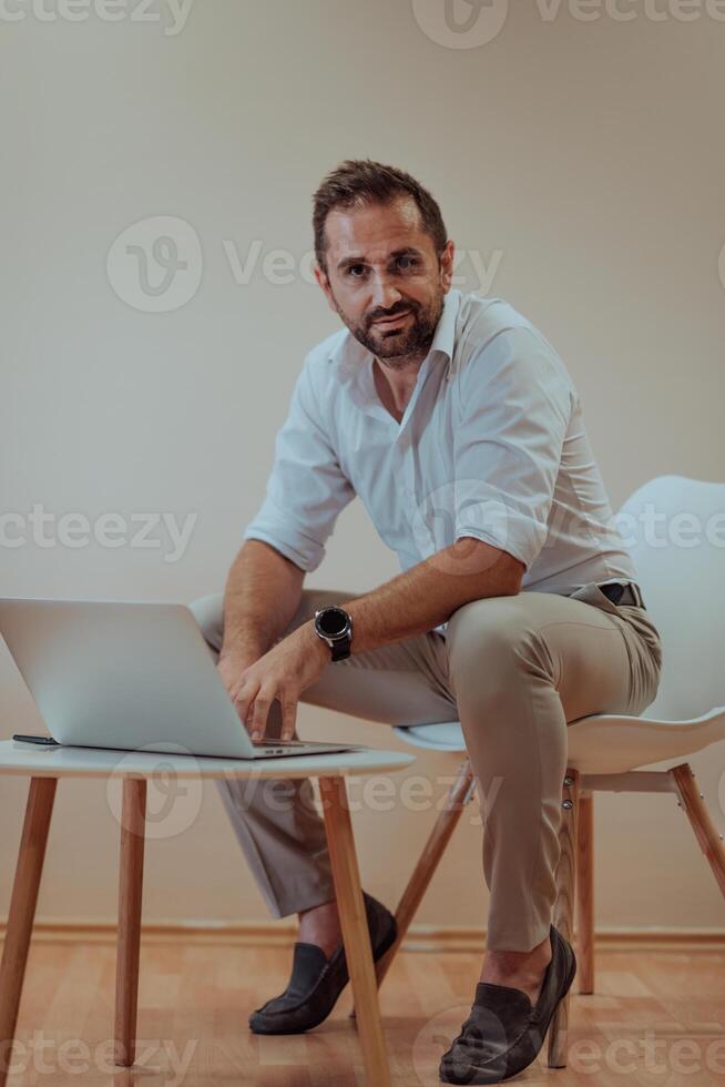 A confident businessman sitting and using laptop with a determined expression, while a beige background enhances the professional atmosphere, showcasing his productivity and expertise. photo