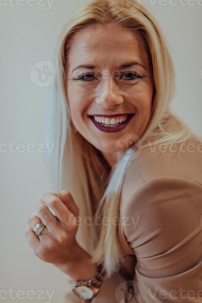 A confident and successful businesswoman, with a wide smile, strikes a pose in front of a beige background, exuding professionalism and elegance photo