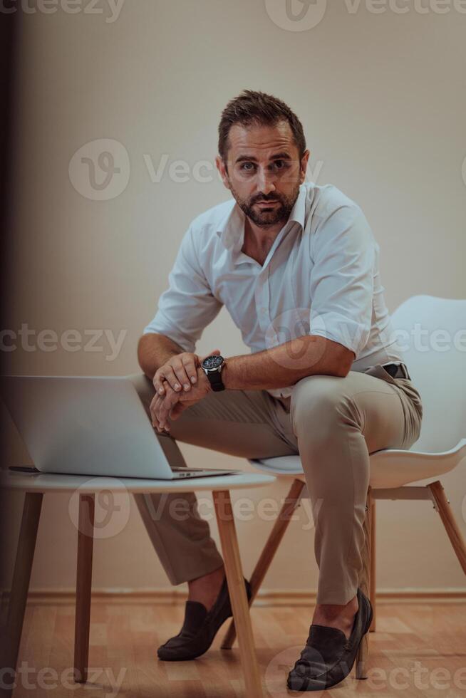 A confident businessman sitting and using laptop with a determined expression, while a beige background enhances the professional atmosphere, showcasing his productivity and expertise. photo