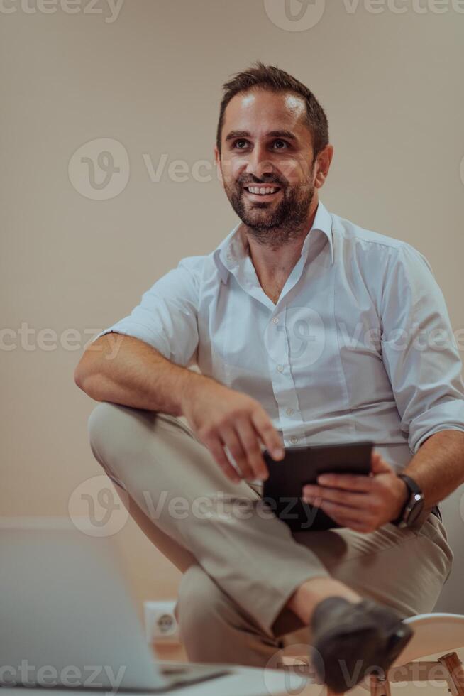 A confident businessman sitting and using tablet with a determined expression, while a beige background enhances the professional atmosphere, showcasing his productivity and expertise. photo