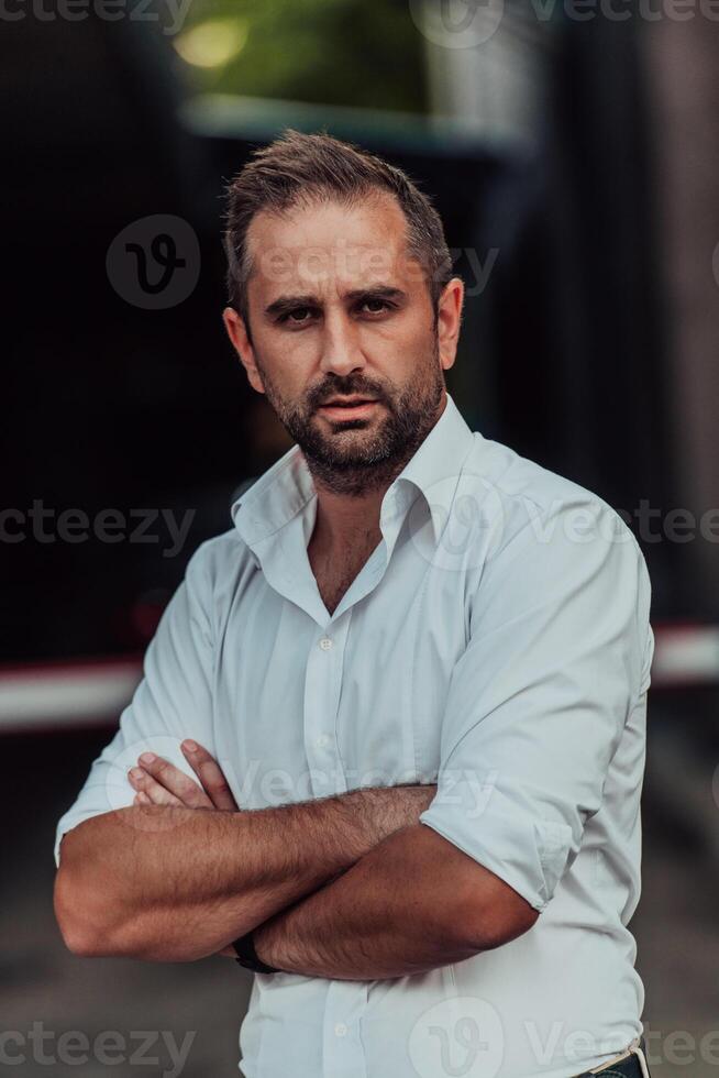 A successful businessman in a white shirt with crossed arms posing outdoors photo