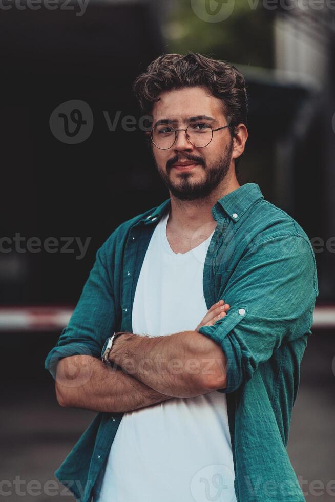 A successful young businessman in a shirt, with crossed arms, poses outdoors, confident expression on his face. photo