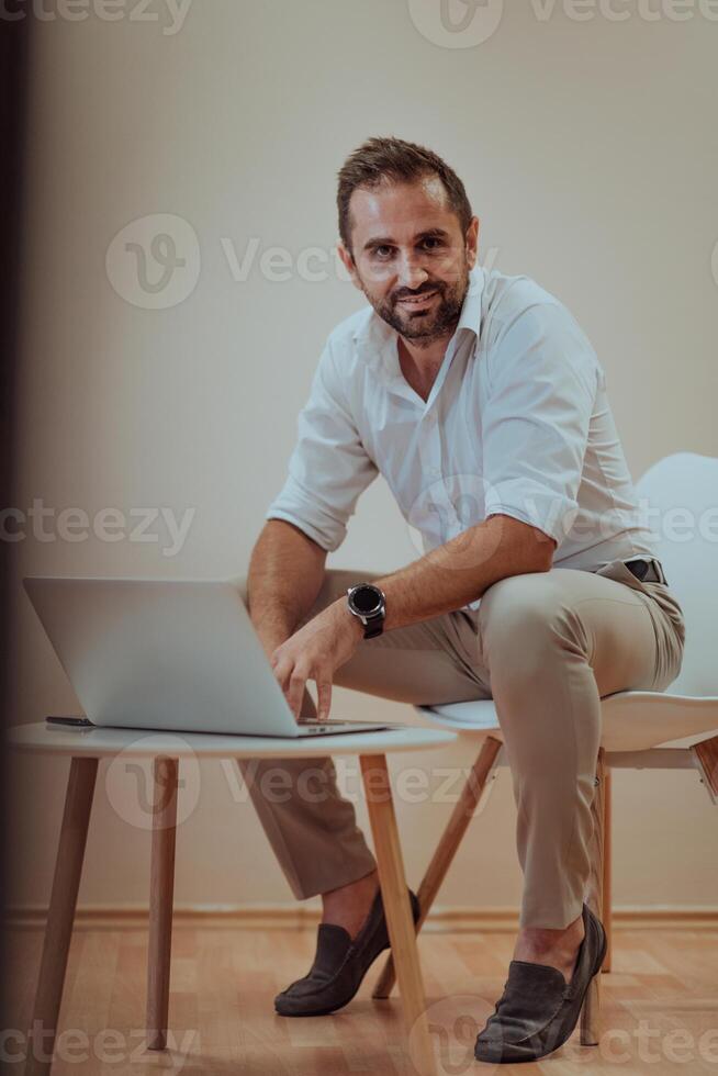 A confident businessman sitting and using laptop with a determined expression, while a beige background enhances the professional atmosphere, showcasing his productivity and expertise. photo
