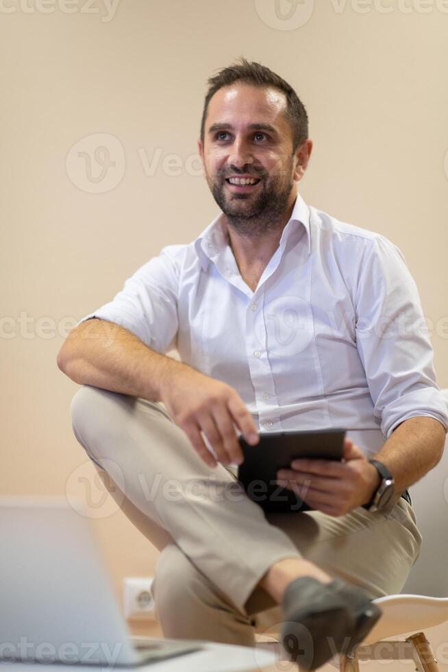 A confident businessman sitting and using laptop with a determined expression, while a beige background enhances the professional atmosphere, showcasing his productivity and expertise. photo