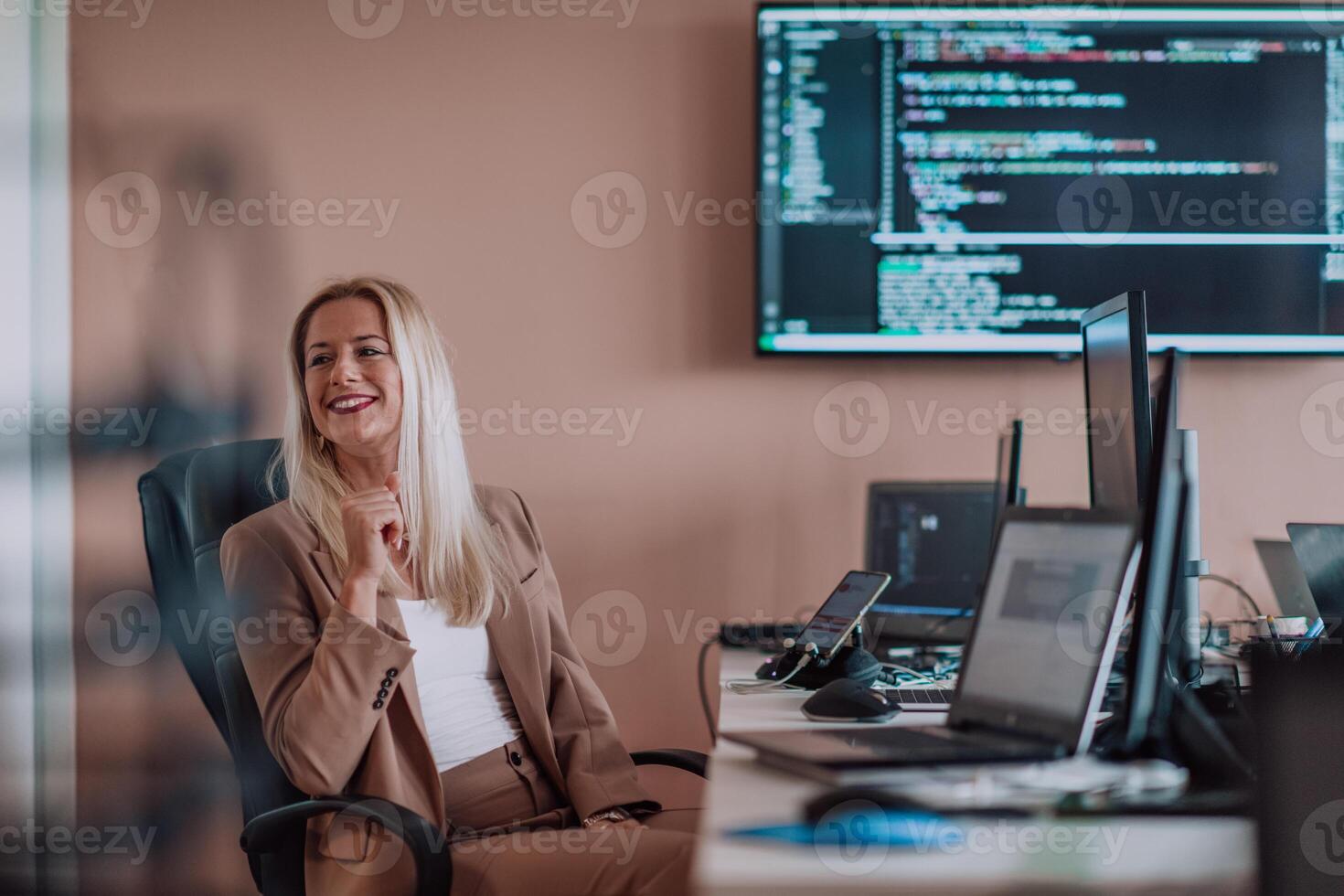 A businesswoman sitting in a programmer's office surrounded by computers, showing her expertise and dedication to technology. photo