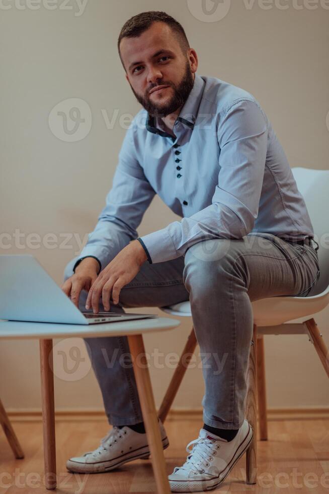 A confident businessman sitting and using laptop with a determined expression, while a beige background enhances the professional atmosphere, showcasing his productivity and expertise. photo