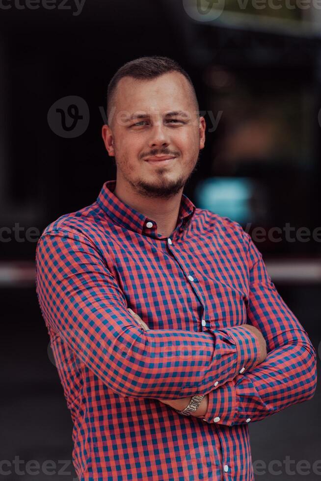 A successful young businessman in a shirt, with crossed arms, poses outdoors, confident expression on his face. photo