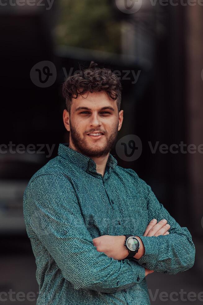 A successful young businessman in a shirt, with crossed arms, poses outdoors, confident expression on his face. photo