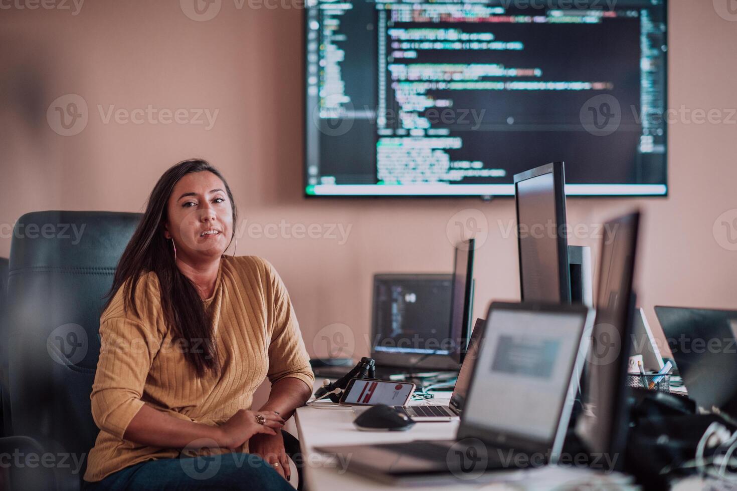 A businesswoman sitting in a programmer's office surrounded by computers, showing her expertise and dedication to technology. photo
