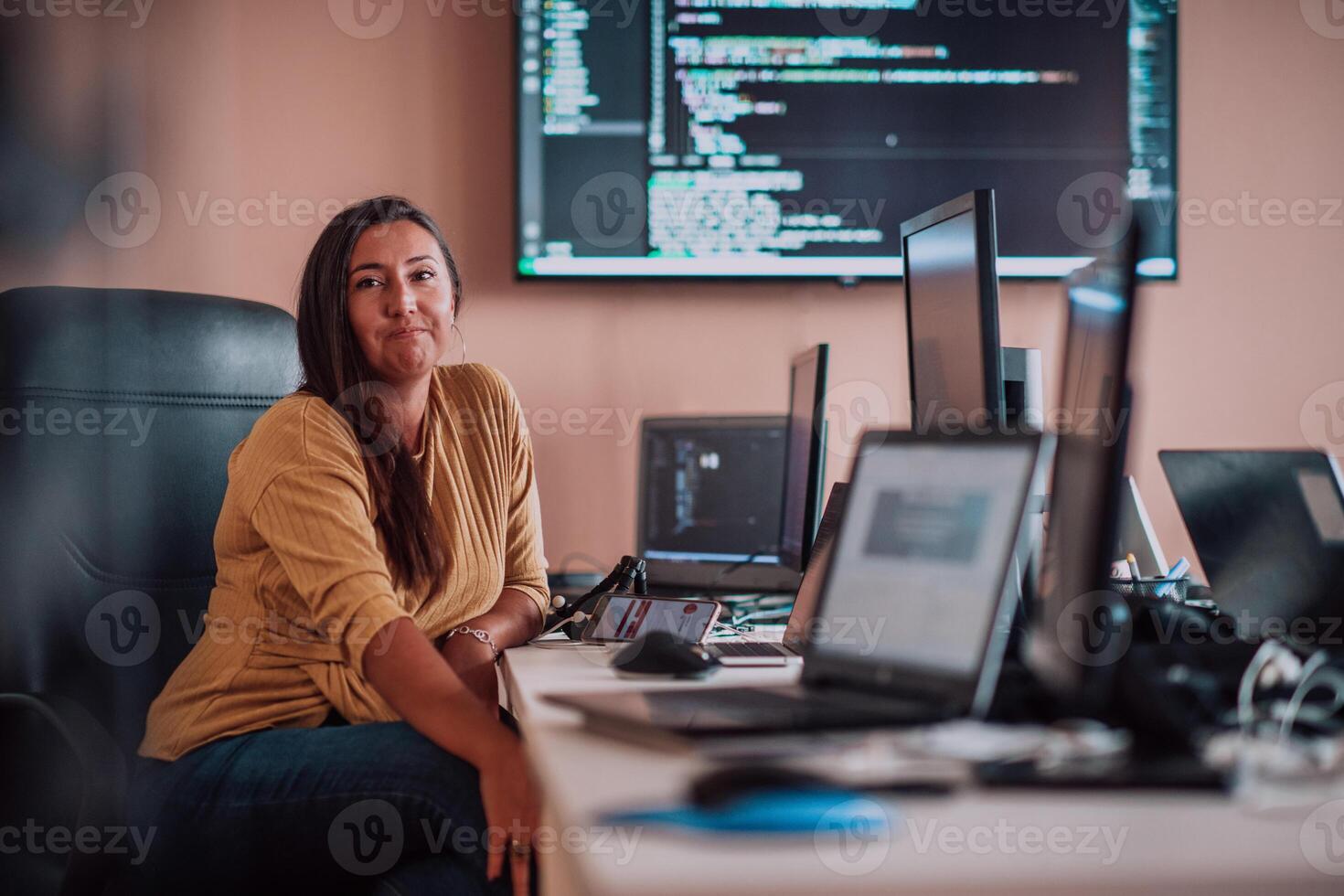 A businesswoman sitting in a programmer's office surrounded by computers, showing her expertise and dedication to technology. photo