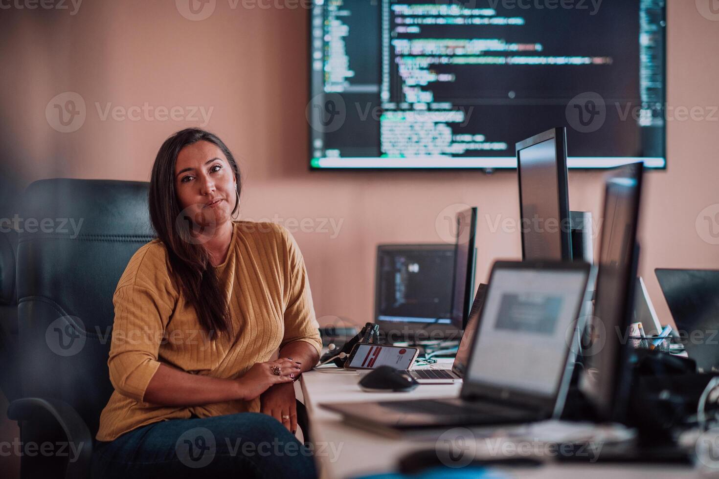 A businesswoman sitting in a programmer's office surrounded by computers, showing her expertise and dedication to technology. photo