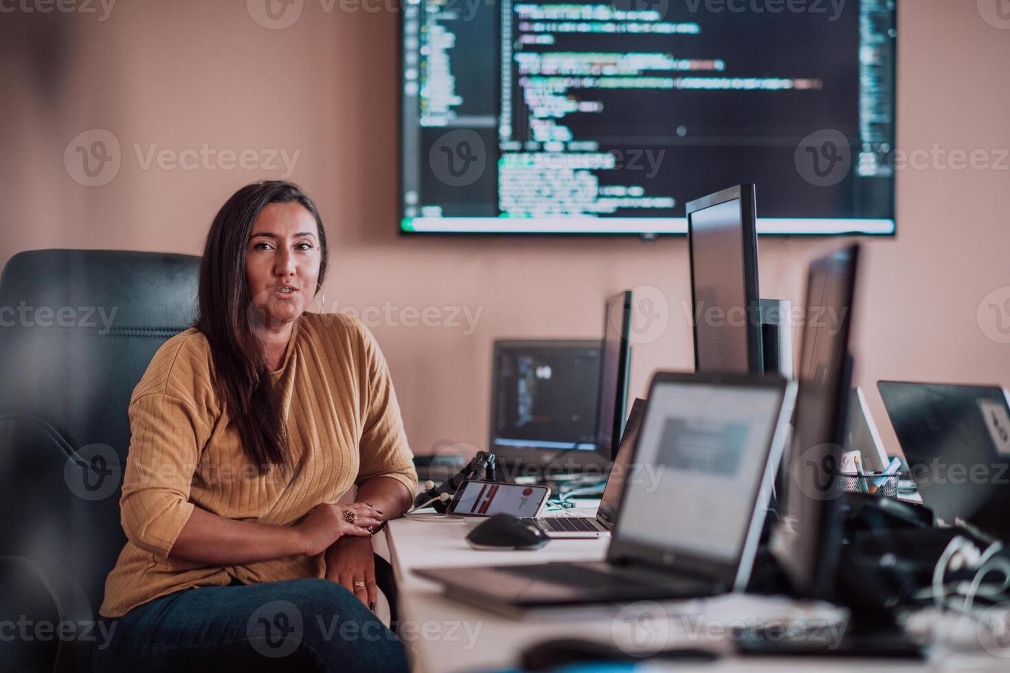 A businesswoman sitting in a programmer's office surrounded by computers, showing her expertise and dedication to technology. photo
