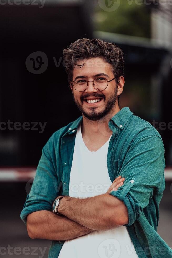 A successful young businessman in a shirt, with crossed arms, poses outdoors, confident expression on his face. photo