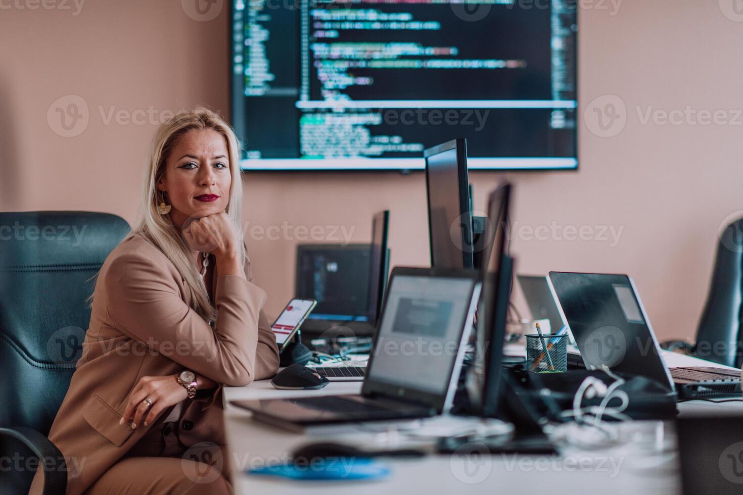 A businesswoman sitting in a programmer's office surrounded by computers, showing her expertise and dedication to technology. photo