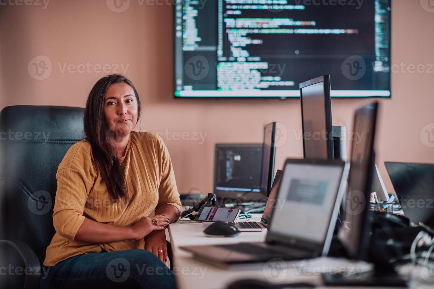 A businesswoman sitting in a programmer's office surrounded by computers, showing her expertise and dedication to technology. photo