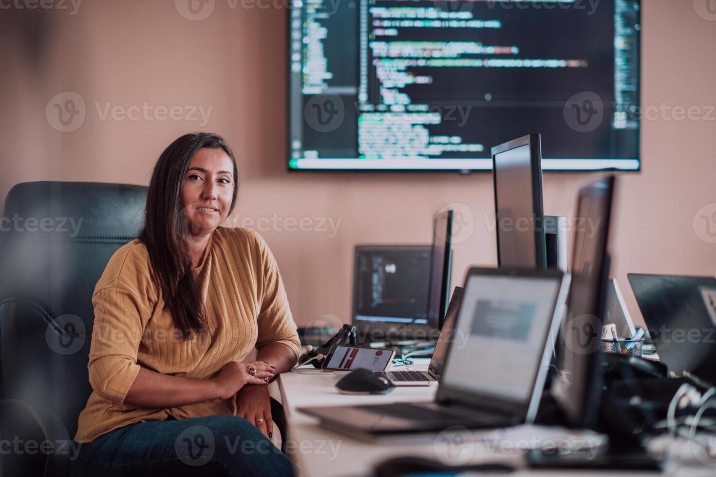 A businesswoman sitting in a programmer's office surrounded by computers, showing her expertise and dedication to technology. photo