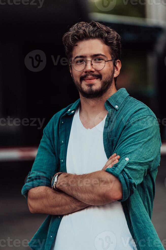 A successful young businessman in a shirt, with crossed arms, poses outdoors, confident expression on his face. photo