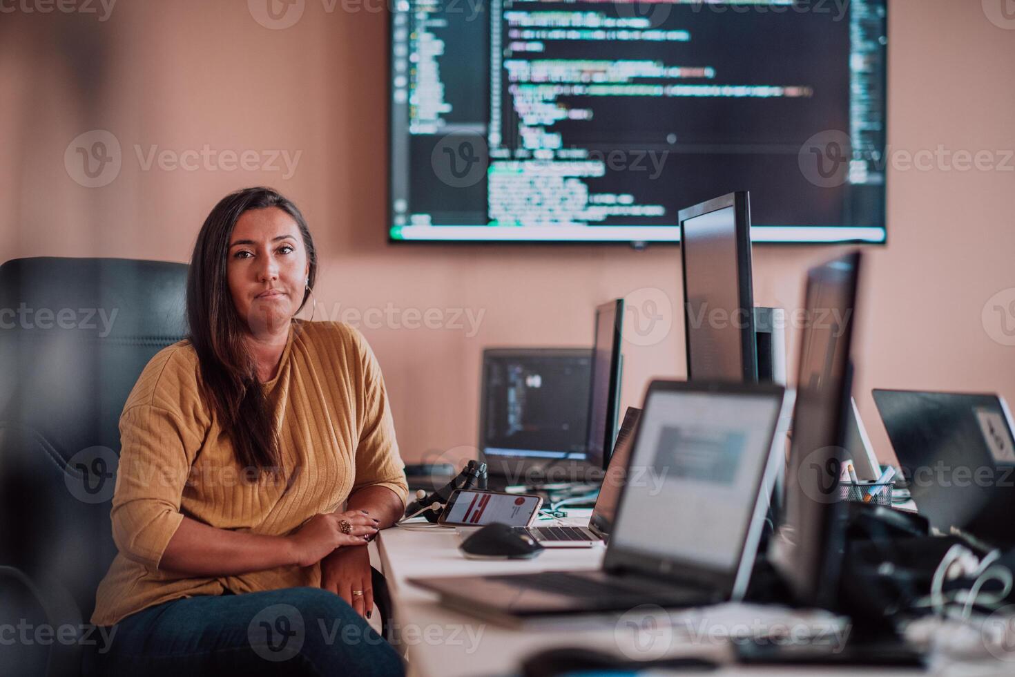 A businesswoman sitting in a programmer's office surrounded by computers, showing her expertise and dedication to technology. photo