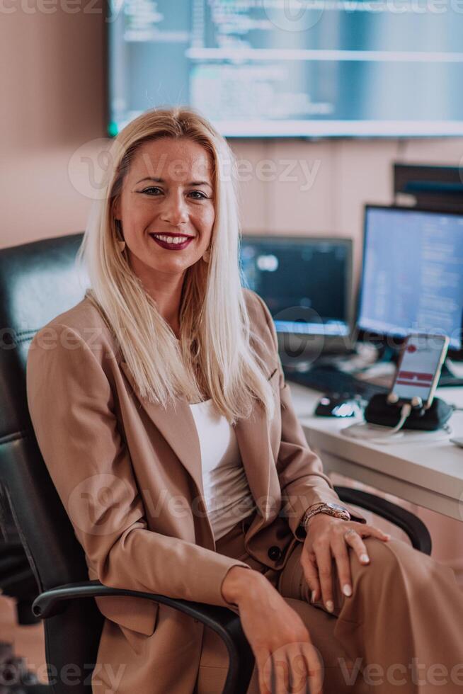 A businesswoman sitting in a programmer's office surrounded by computers, showing her expertise and dedication to technology. photo