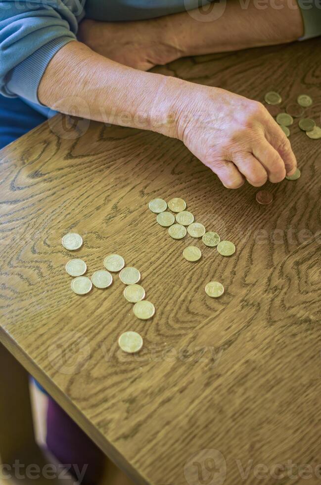 senior female sitting miserably at the table at home and counting coins. High quality photo