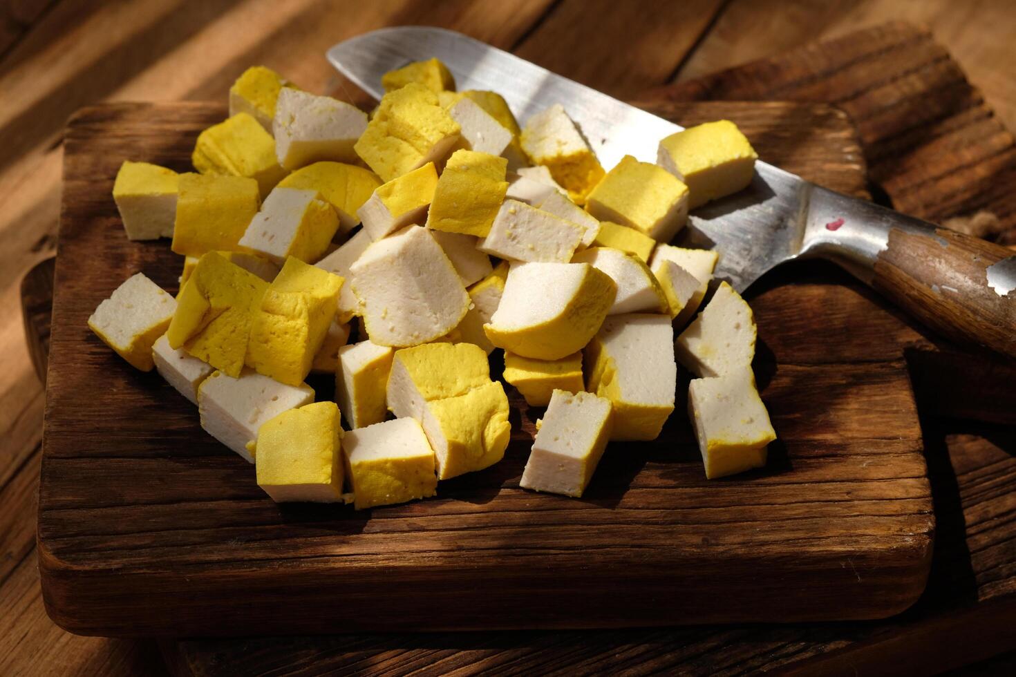 sliced yellow tofu on a teak wood cutting board. stainless steel blade. soy bean products. photo