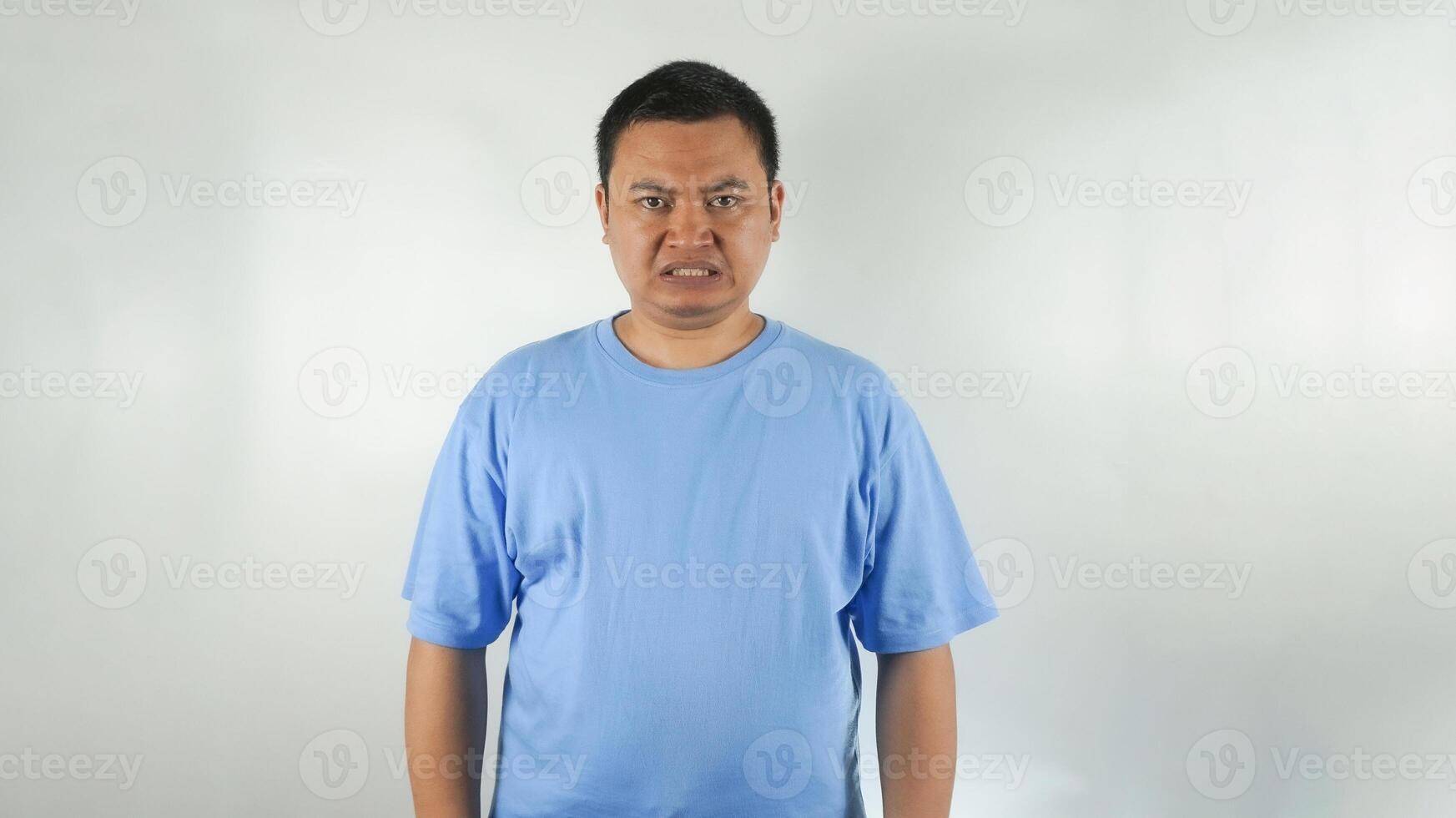 A young Indonesian man wearing a blue t-shirt with a frown facing forward photo