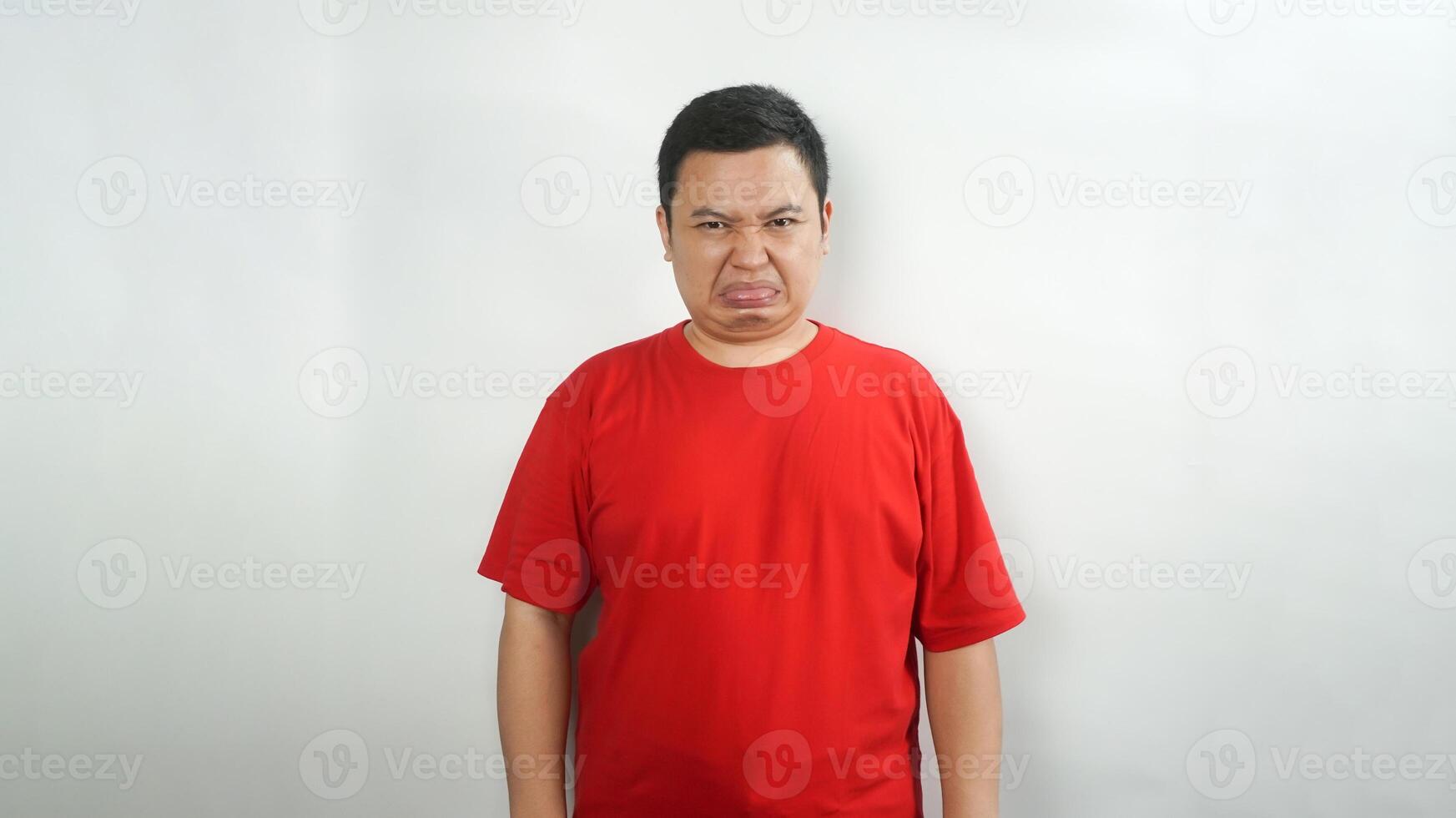 A young Indonesian man wearing a red t-shirt with a disgusted face facing forward photo