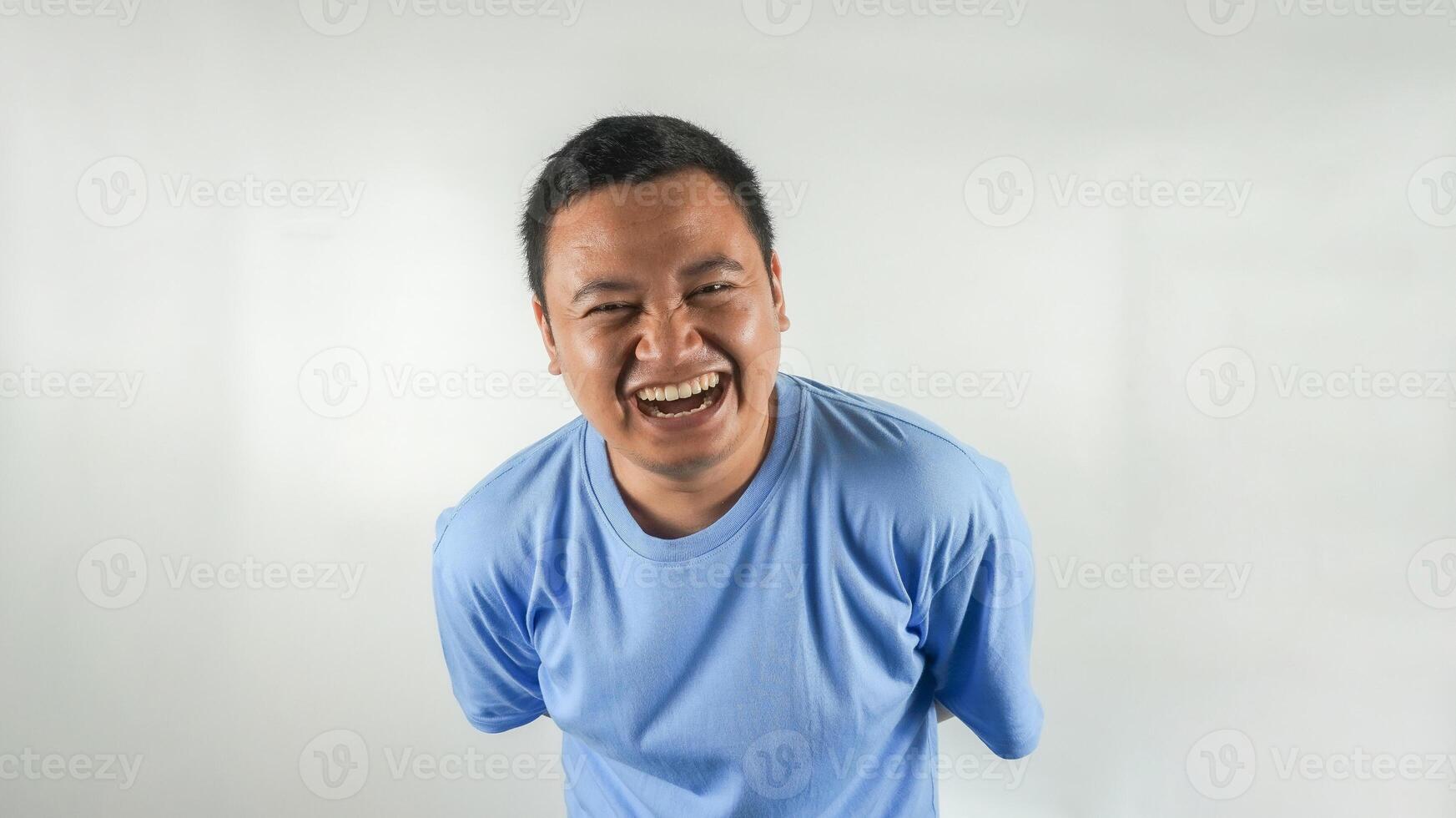A young Indonesian man wearing a blue t-shirt is laughing facing forward photo