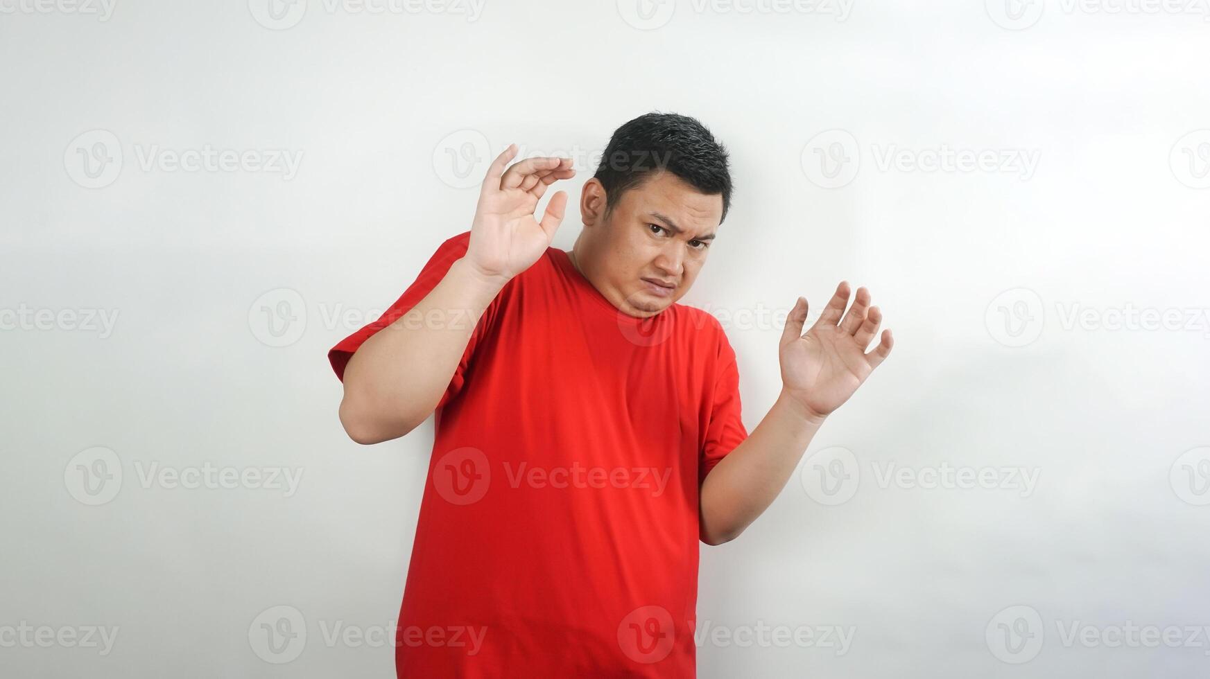 A young Indonesian man wearing a red t-shirt with a scared face facing forward photo