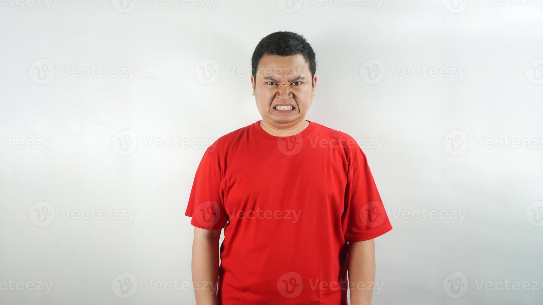 A young Indonesian man wearing a red t-shirt with an angry face facing forward photo