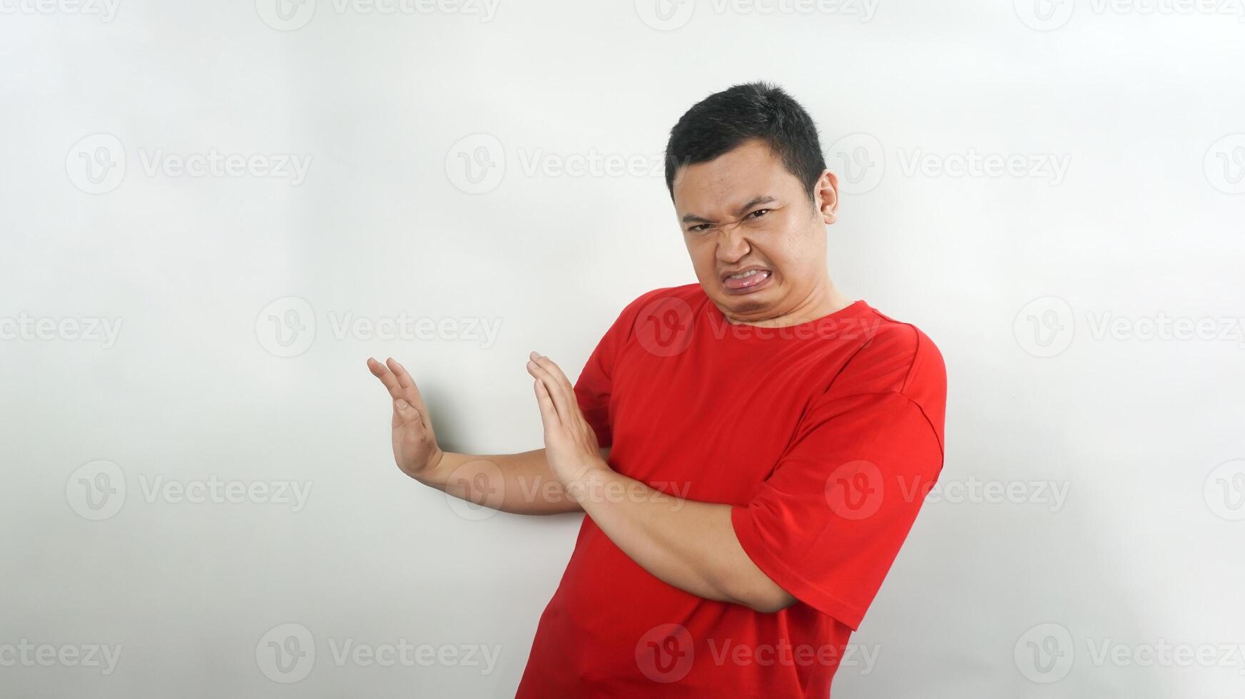 A young Indonesian man wearing a red t-shirt with a disgusted face facing forward photo